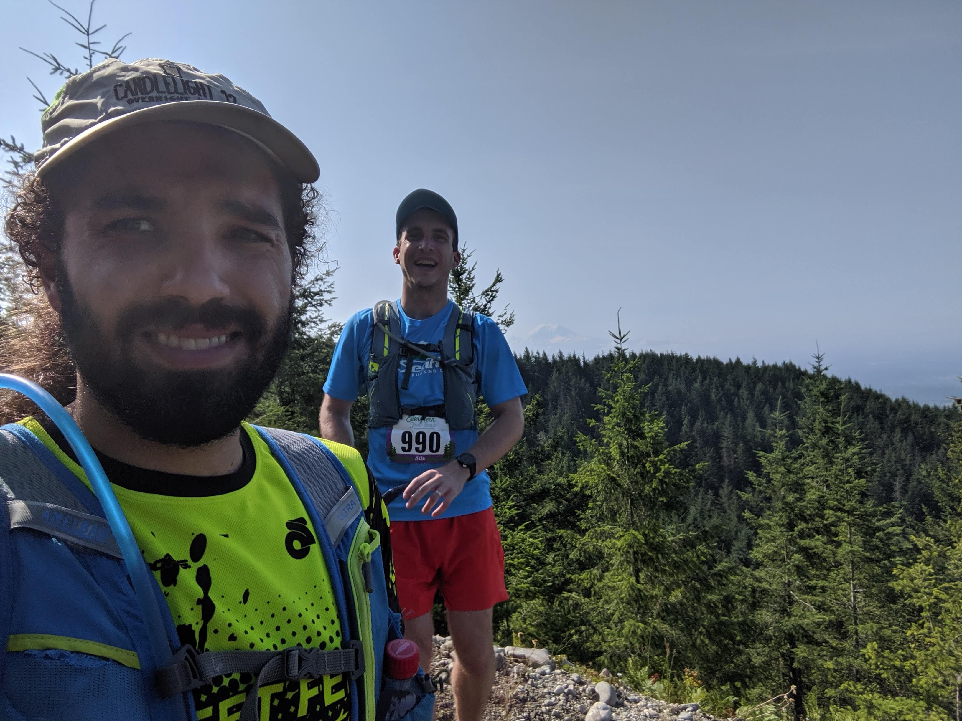 Selfie of Bobby and me at the top of a hill, with coniferous trees in the background and Mount Ranier barely visible through the haze